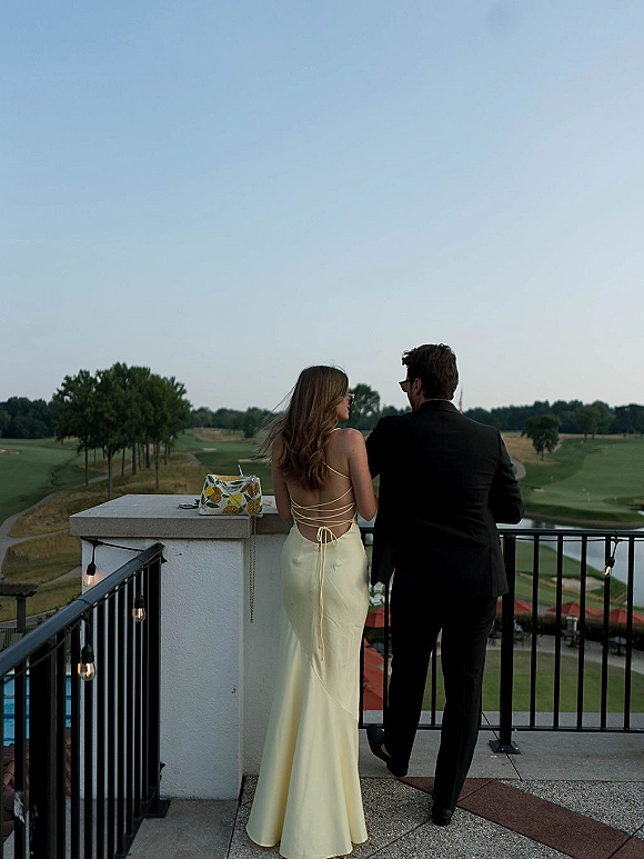 Couple portrait of bride and groom from behind in sunglasses, bride in a backless dress, overlooking a golf course from a balcony