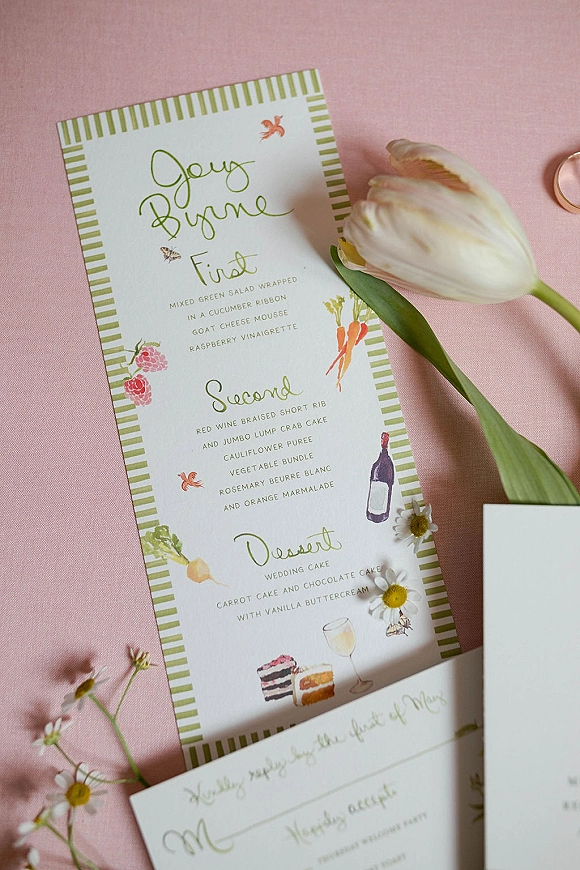 Wedding menu card with illustrated wedding menu design, calligraphy text, striped border, and tulip and daisy accents on pink fabric backdrop