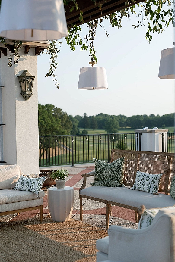 Outdoor lounge seating with neutral sofa, patterned throw pillows, chairs and rug under pendant and string lights on a terrace patio