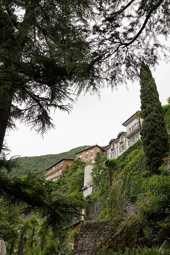 Wedding venue exterior with ivy vines on a stone wall, balconies and windows, framed by palm trees and a cypress on a misty hillside