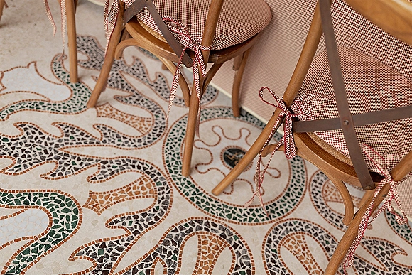 Wedding chair decor with gingham wedding decor, featuring red gingham chair cushions and ribbon bows on wood chairs over mosaic tile floor