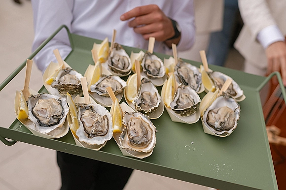 Wedding oyster bar tray with oysters on the half shell and lemon wedges, served in paper boats by a caterer in a white shirt