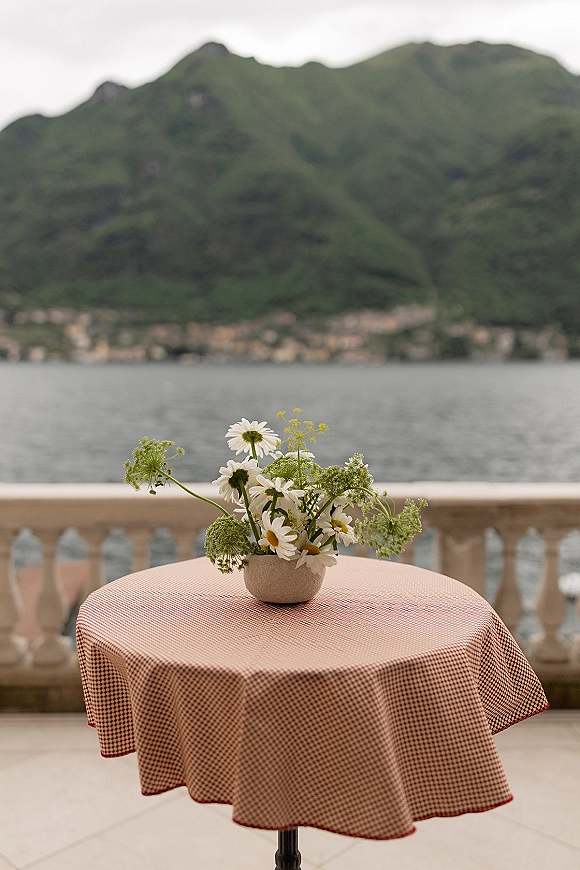 Table centerpiece wildflower table centerpiece with daisies in a small ceramic vase on a red gingham cloth, set on a terrace by a lake and mountains