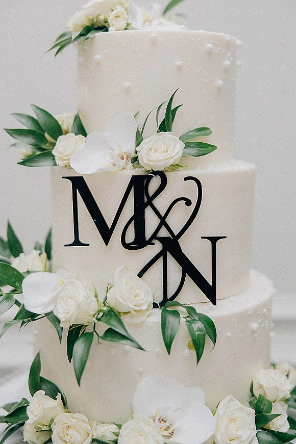 Wedding cake with three tier wedding cake design in white buttercream, adorned with cascading white roses and orchids against white drapery