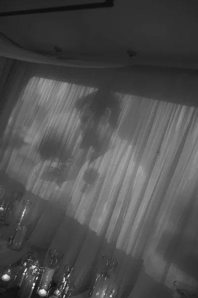 Wedding couple silhouette kissing on an indoor wall, bride and groom shadow framed by sheer drapery and candlelit glass cylinder vases