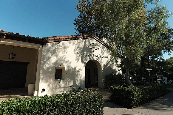 Wedding venue exterior with a Spanish style wedding venue arched entryway, stucco walls and terracotta roof tiles under a blue sky