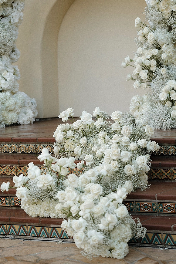 Ceremony floral installation with white rose ceremony flowers framing an arched doorway, with hydrangeas and baby's breath lining tiled steps