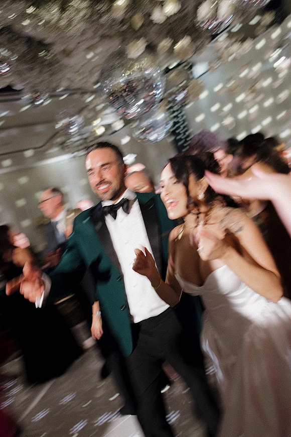 Wedding reception dancing as the bride and groom dancing under disco balls and string lights, surrounded by guests on a lively indoor dance floor