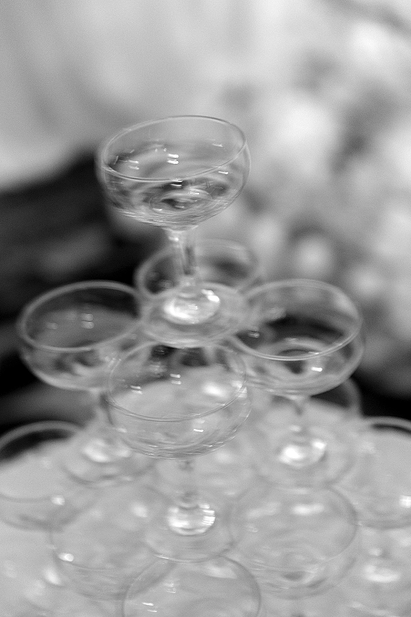 Champagne tower wedding display of stacked coupe glasses on a reception table, with a softly blurred background for an elegant toast setup
