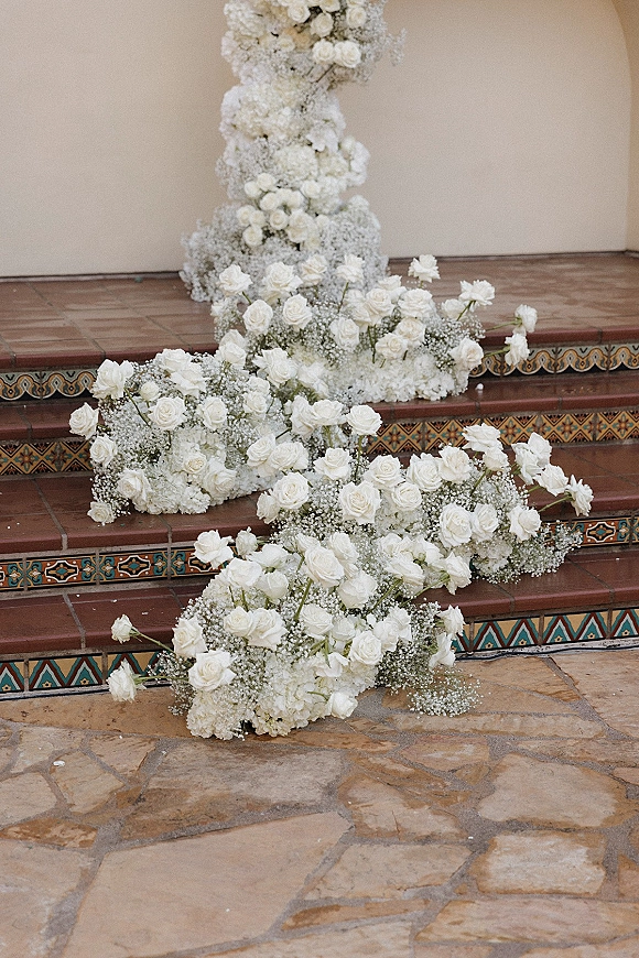 Wedding staircase florals, a staircase floral installation of white roses and hydrangeas cascading along tiled steps beside a stucco wall