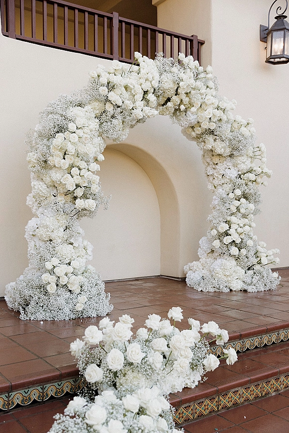 Wedding floral arch with a white flower arch of roses, hydrangeas and baby’s breath on tiled steps by a stucco doorway