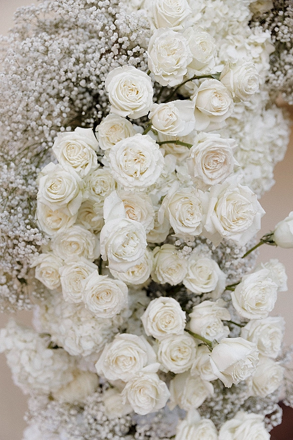 White rose bouquet with baby's breath bouquet accents and greenery stems, hand-tied and round against a neutral backdrop