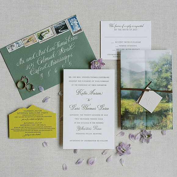 Invitation suite with wedding invitation suite cards, calligraphy envelope, vintage postage, vellum wrap, twine, and rings on linen background