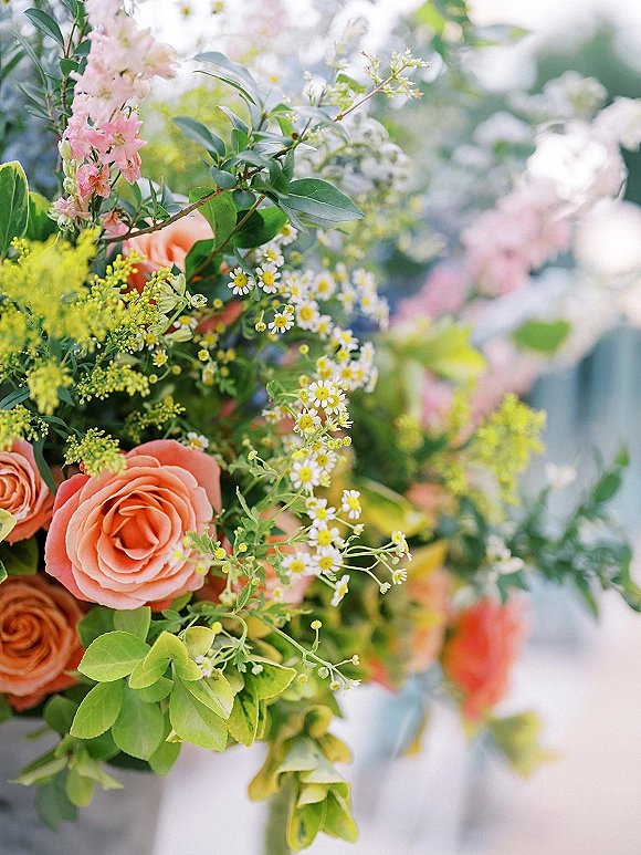 Wedding bouquet with peach roses and chamomile daisies, hand-tied with greenery and pink blossoms against soft outdoor bokeh greenery