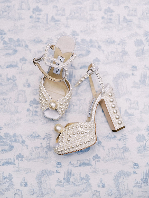 Bridal shoes, pearl wedding heels with ankle straps and open toes, arranged on blue and white toile fabric flat lay background