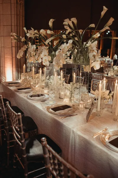Reception tablescape with long banquet table decor, styled with white orchids, in a warm uplit ballroom with a mirrored wall.