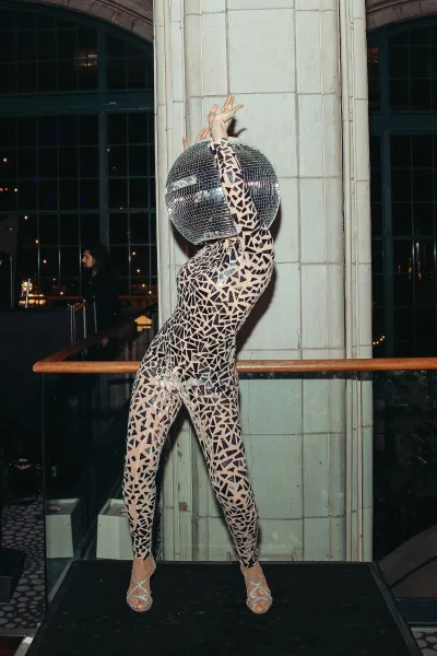 Wedding entertainment shines as a reception performer wearing a disco ball helmet under arched windows near the DJ booth and city lights.