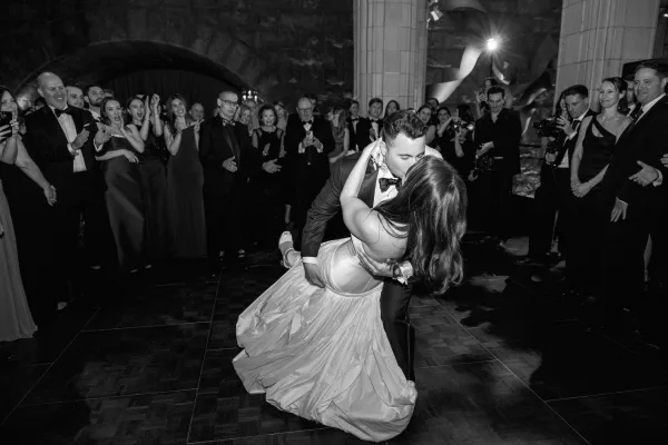 Wedding first dance as the groom dips bride under a stone archway with warm uplighting, framed by columns on the dance floor.