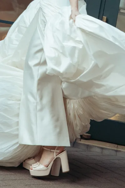 Bridal shoes styled as platform wedding heels, peeking from beneath wide-leg pants, showing the pairing within a cohesive bridal ensemble.