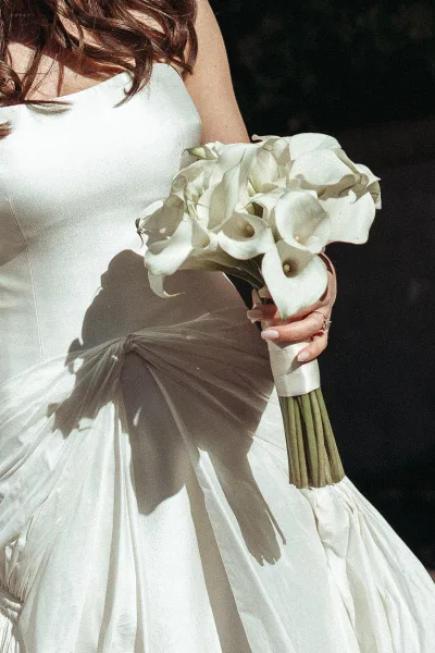 Calla lily bouquet, bride holding bouquet with sleek long stems and a satin ribbon wrap against a dark background