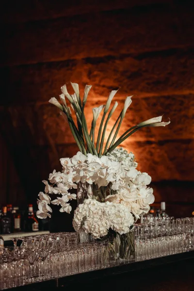 Floral arrangement for wedding bar decor featuring orchids on a bar counter set against a rustic stone wall