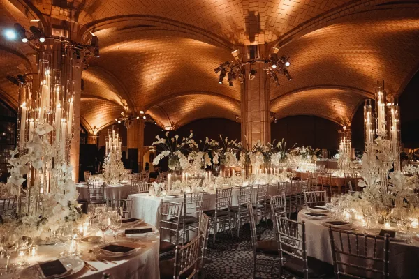 Reception tablescape with candlelit reception decor and white orchids beneath a vaulted ceiling with stone arches and columns.