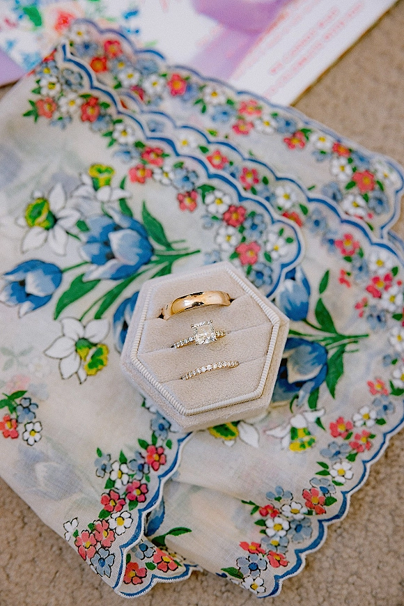 Wedding rings displayed in velvet ring box styling, with gold band and diamond rings on floral lace handkerchief beside stationery