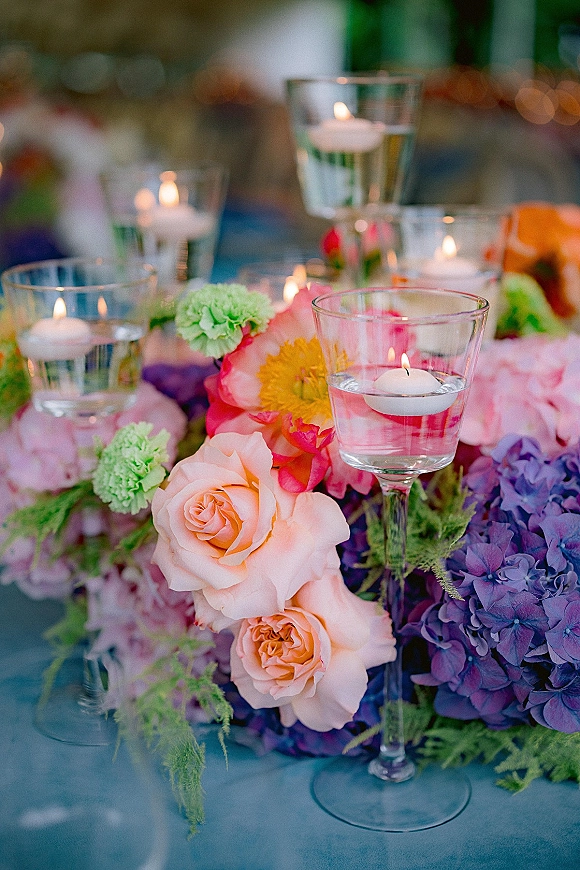 Wedding centerpiece with floating candle centerpiece in glass holders, roses, hydrangea and greenery on a table with blurred reception lights
