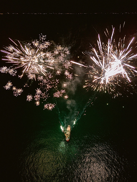 Wedding fireworks bursting over ocean water beside a boat, lighting the night sky during a wedding fireworks display celebration
