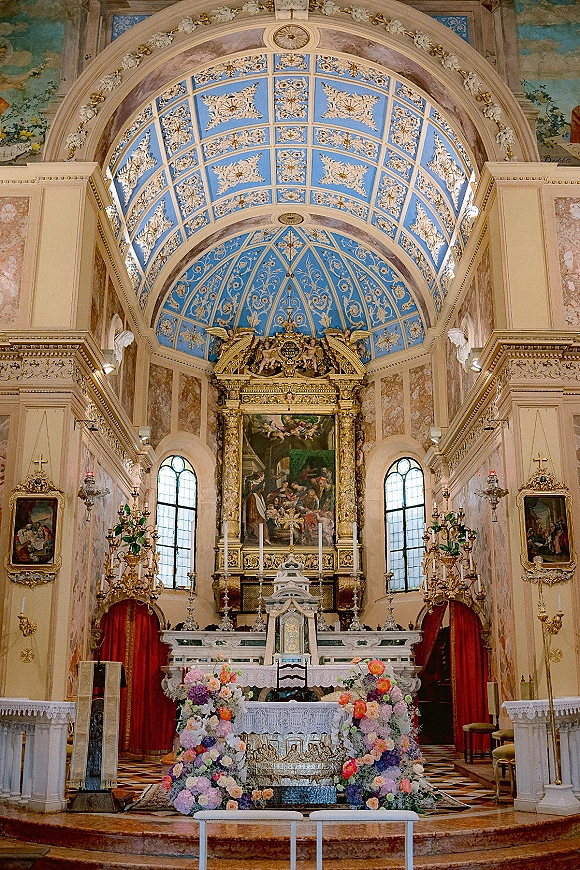 Church ceremony altar with wedding altar flowers, candles and gilded candelabras beneath a blue frescoed dome in an ornate chapel interior