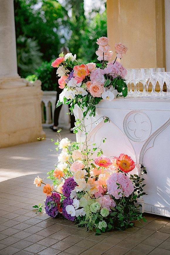 Wedding bar decor with wedding bar flowers cascading over the counter beside champagne flutes on an outdoor stone terrace with columns