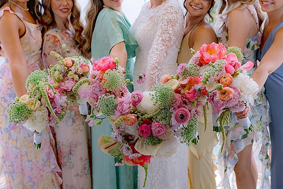 Bridesmaid bouquets in a colorful bridesmaid bouquets lineup, with peonies, ranunculus and roses wrapped in white ribbon outdoors in daylight