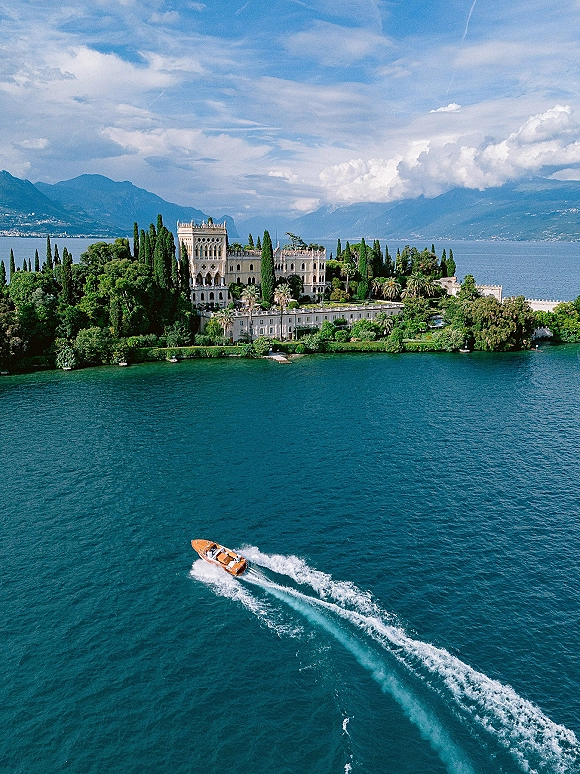 Wedding venue aerial overlooking a lakefront wedding venue with historic villa, formal gardens, cypress trees, and a motorboat on the lake below