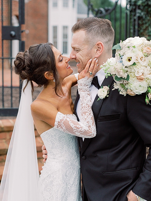 Couple portrait of bride and groom close up, forehead to forehead as she touches his face, showing ring by iron gate and brick steps
