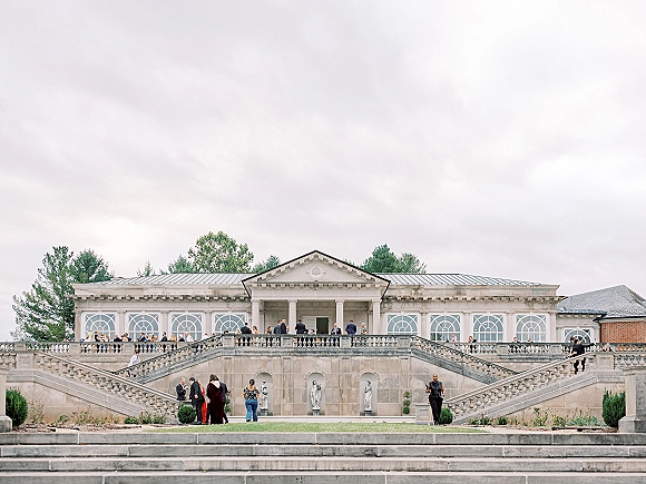 Wedding venue exterior with a grand staircase and stone balustrade, statues and columns framing arched windows under a cloudy sky