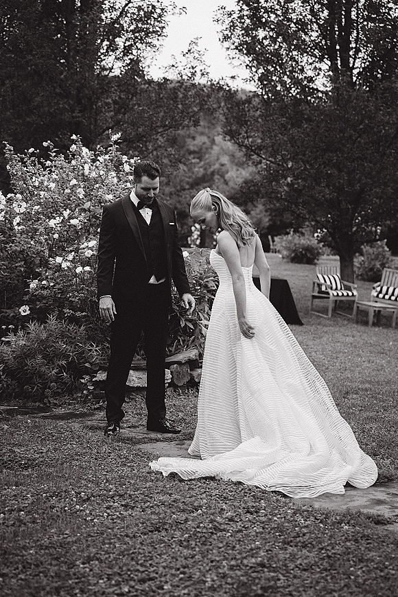 Couple portrait in a black and white wedding portrait style, bride in a strapless gown with train and groom in tuxedo in a garden setting
