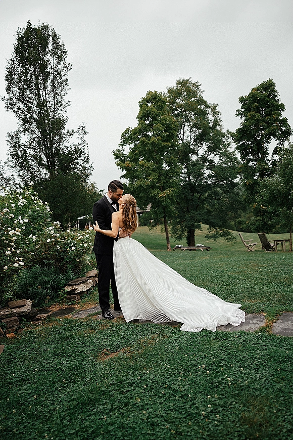 Wedding kiss portrait of the bride and groom kissing in a romantic dip, her strapless gown and long train flowing by white flower bushes