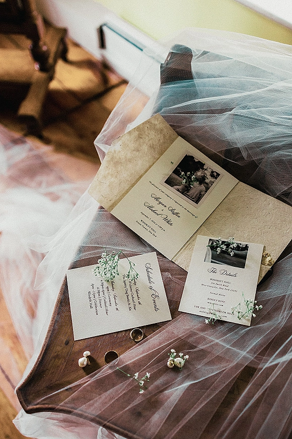 Invitation suite wedding invitation flat lay with RSVP, envelope, vellum veil, gold bands, pearl studs, baby's breath on a wooden chair