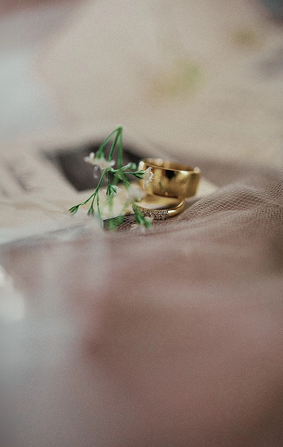Wedding rings with gold wedding bands and a diamond eternity band on tulle fabric, accented by small white flowers on soft neutral fabric