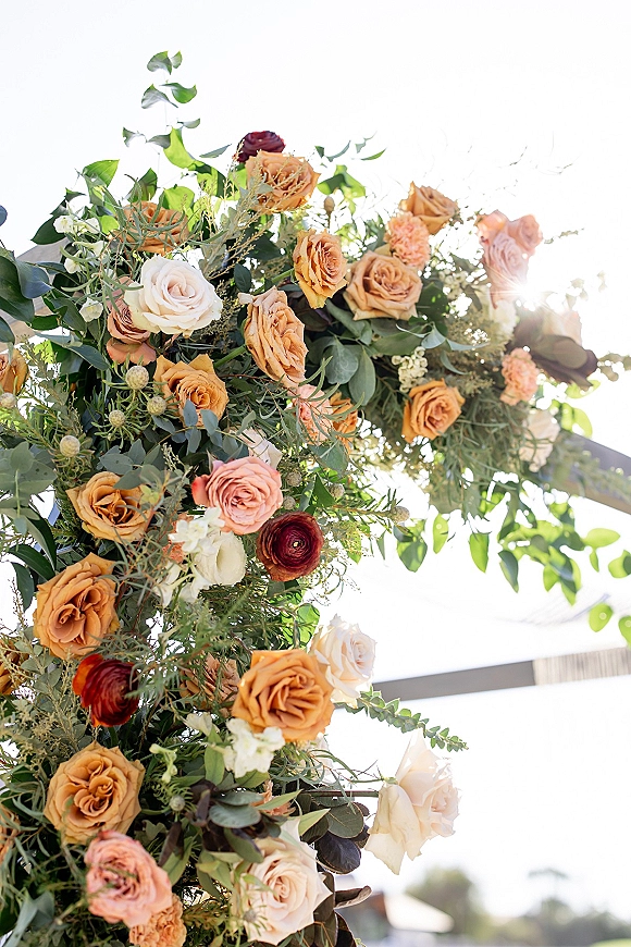 Wedding floral arch with ceremony arch flowers, roses and ranunculus with eucalyptus greenery on an arch frame against sunlit sky