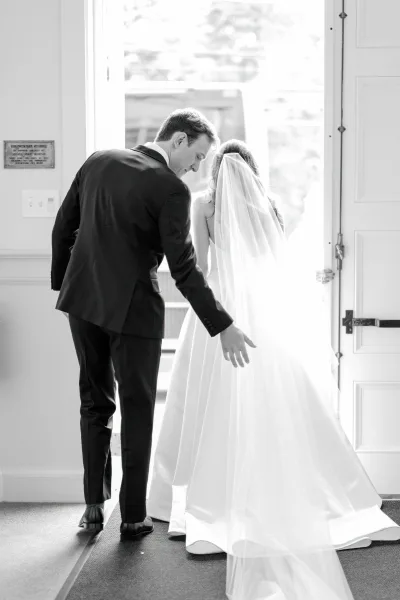Couple portrait of bride and groom walking away, groom guiding her through an open doorway, long veil and train lit by window light