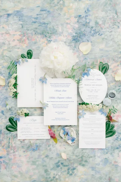 Invitation suite wedding invitation flat lay with deckled cards, envelopes, wax seal, rings in ring box, and peony on a watercolor backdrop