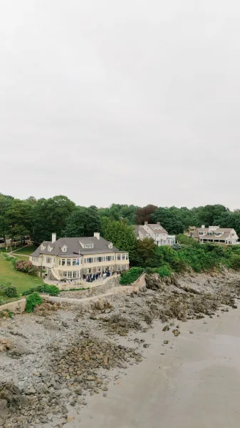 Wedding venue exterior at a coastal wedding venue with patio railing and American flag overlooking rocky shoreline, beach, and ocean under overcast sky