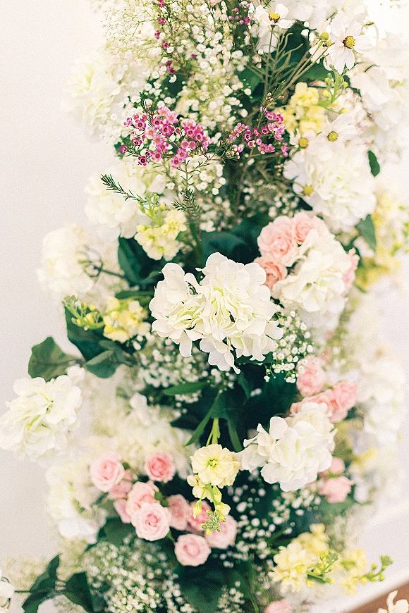 Wedding floral arrangement on a ceremony floral pillar with pink roses and airy baby’s breath in soft natural light against a pale wall