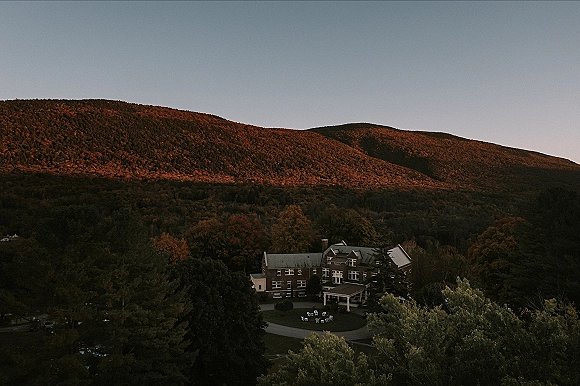 Wedding venue exterior with outdoor ceremony chairs along the driveway, framed by a portico and autumn trees on a mountain hillside
