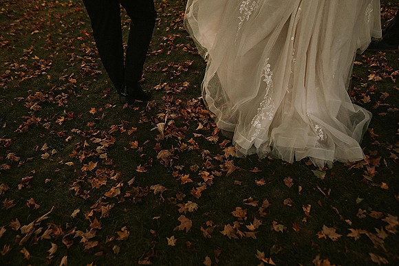 Wedding couple walking away, bride and groom walking away as lace appliqué tulle skirt sways over autumn leaves on grass lawn