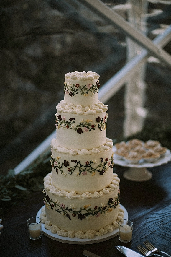 Wedding cake with four tier wedding cake design, piped frosting and floral icing on a stand with votive candles on a wood table