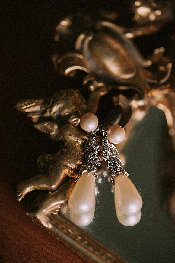 Bridal earrings with pearl drop earrings in diamond leaf settings displayed on a mirror beside a vintage brass jewelry box on wood table