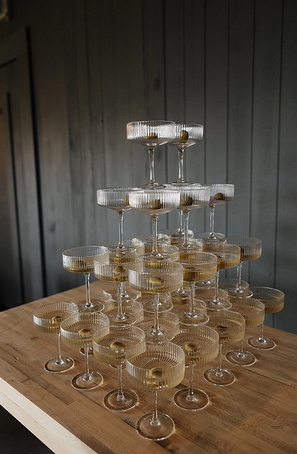 Champagne tower of stacked coupe glasses filled with golden champagne on a wood table against a dark paneled wall