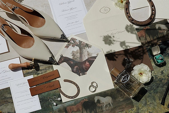 Wedding invitation suite and wedding stationery flat lay with calligraphy cards, wax seal, rings, perfume, and shoes on a painted tabletop with botanical shadows